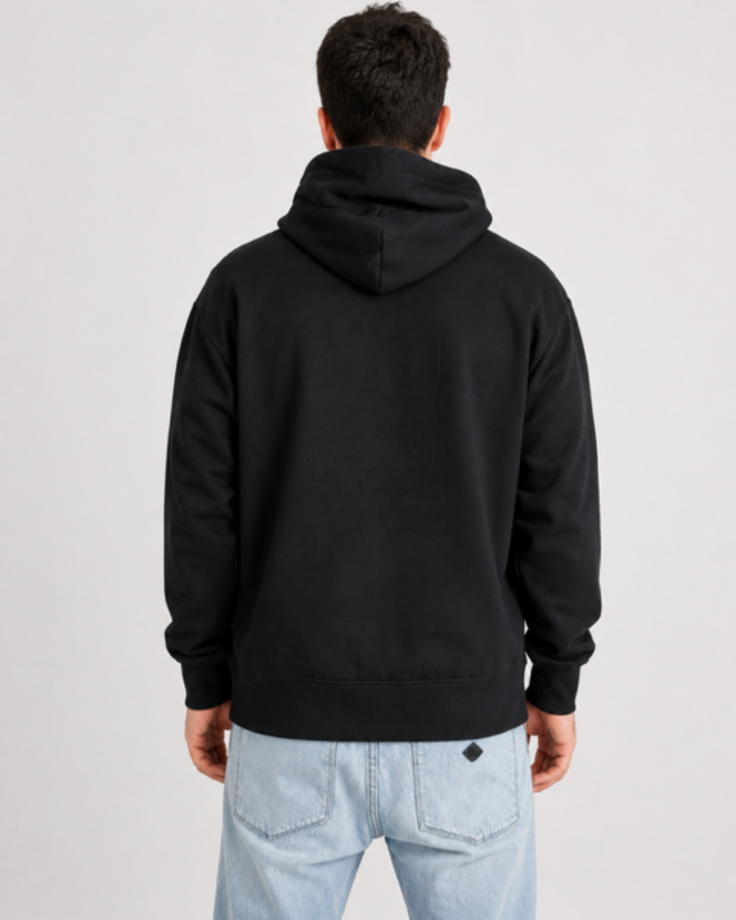 Person wearing a black hoodie and light blue jeans on a plain background